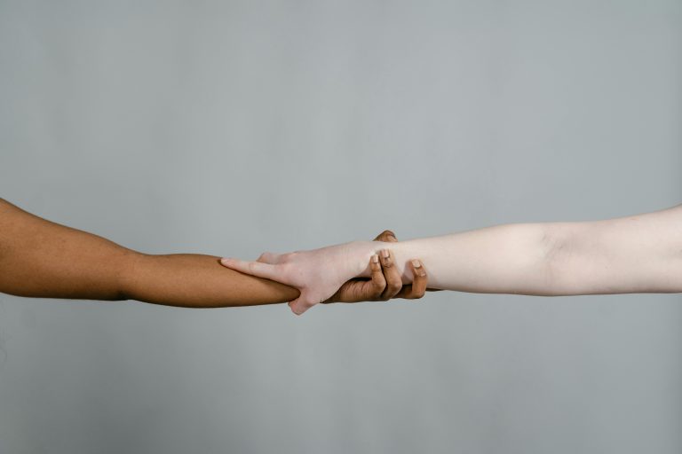 Twee armen (donker en blank) die elkaar vasthouden - 🌍 Internationale Dag van de Migrant – 18 december